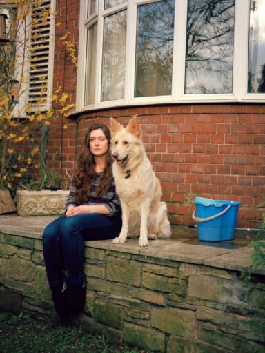 A person and a dog sitting on a stone ledge outside a house Description automatically generated with low confidence